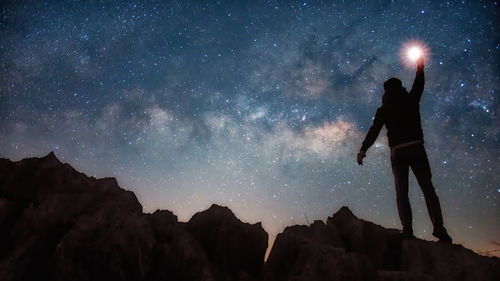 Silhouette person standing on rock against sky at night