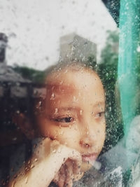 Close-up portrait of boy seen through wet glass window