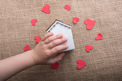 Cropped hand of woman holding model home with red heart shapes on table