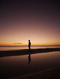 Silhouette of a man walking along the beach during sunset
