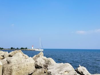 Sailboats on rock by sea against blue sky