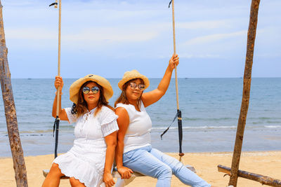 Portrait of friends sitting on beach by sea against sky