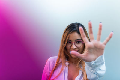 Portrait of smiling woman with glasses showing palm while standing on colorful background