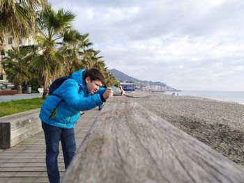 Rear view of boy on shore at beach against sky