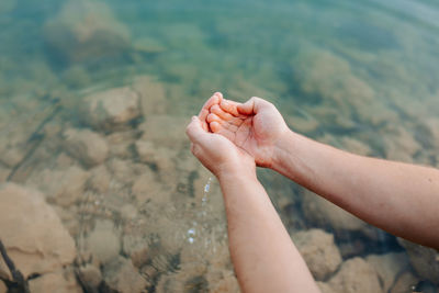 Cropped unrecognizable person hands holding water from transparent lake