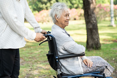 Caregiver help and care asian senior woman patient sitting and happy on wheelchair in park