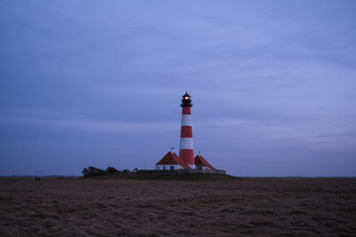 Lighthouse on beach by building against sky