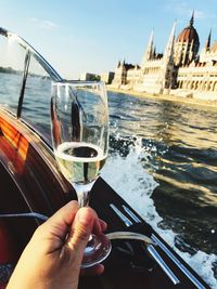 Close-up of hand holding champagne flute while traveling in boat against church