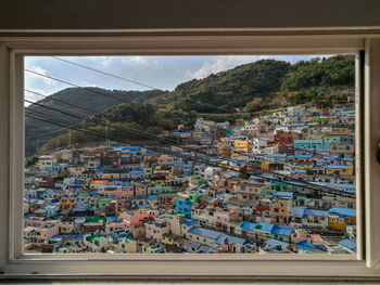 Buildings in city against sky seen through glass window