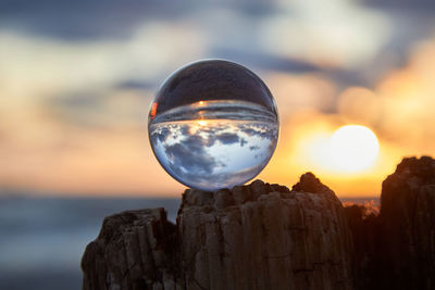 Close-up of crystal ball on rock against sky during sunset