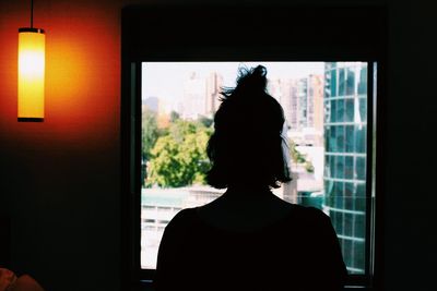Rear view of silhouette woman looking through window