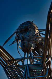 Low angle view of bird perching on metal against blue sky