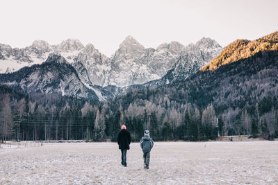 Rear view of people walking on land towards mountain during winter