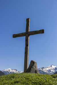 Low angle view of cross on field against clear blue sky