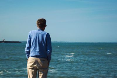 Rear view of man standing by sea against sky