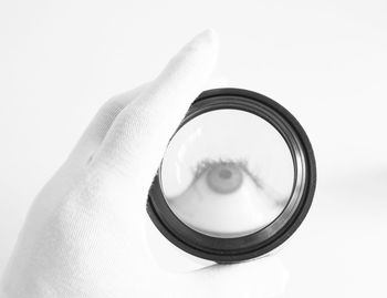 Close-up of hand holding lens over white background