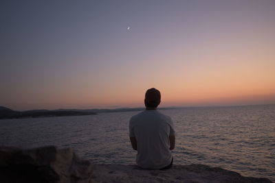 Rear view of man looking at sea against sky during sunset