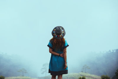 Rear view of woman standing on mountain during foggy weather