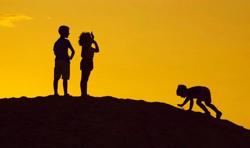 Silhouette friends standing on land against sky during sunset