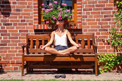 Woman sitting on bench against brick wall