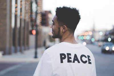 Rear view of young man standing on street against sky during sunset