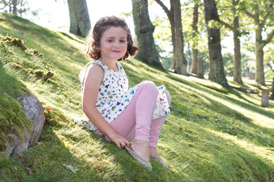 Portrait of smiling girl sitting on grass against trees