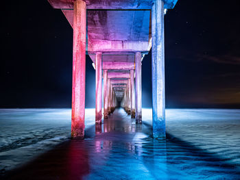 Blue and red lit underside of pier with night sky
