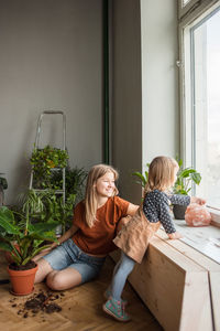 Woman sits and look at window, little girl near points out window.