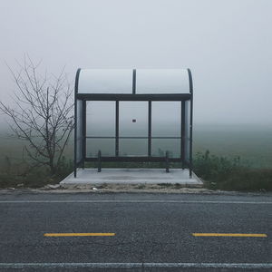 Empty bus stop at roadside by field during foggy weather