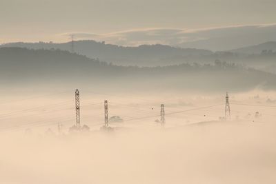 Electricity pylons against mountains in foggy weather