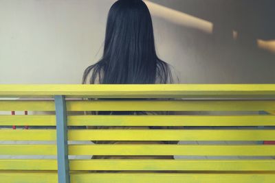 Rear view of woman sitting on bench against wall