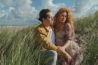 Young couple sitting on field against sky