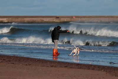 Man with dog on shore at beach against sky