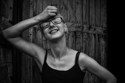 Portrait of smiling young woman standing against wooden wall