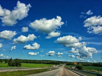 Road passing through field against cloudy sky