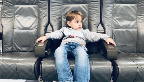 Full length of cute boy sitting on chair in airplane