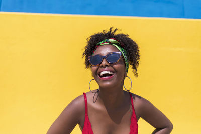 Young woman wearing sunglasses while laughing against wall