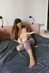 Mom with a baby in her arms sits in the bedroom on the bed.