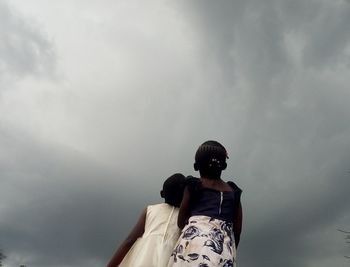 Low angle view of sisters looking at storm clouds