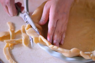 Cropped hands cutting pie dough in kitchen