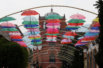 Low angle view of multi colored umbrellas hanging by building against sky