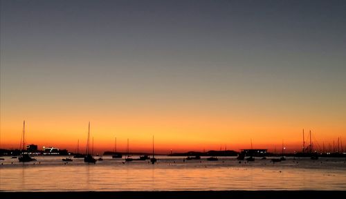 Sailboats in sea against clear sky during sunset