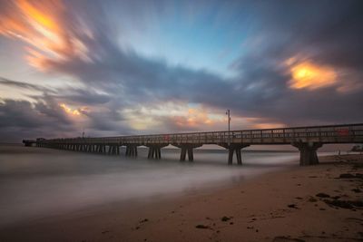 Pier over sea at beach against cloudy sky during sunset