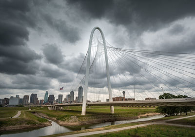 Bridge over river by buildings in city against cloudy sky