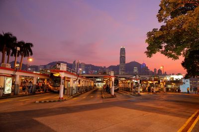 Illuminated street by buildings against sky at night