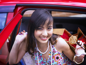 Portrait of smiling young woman holding shopping bags while getting from car
