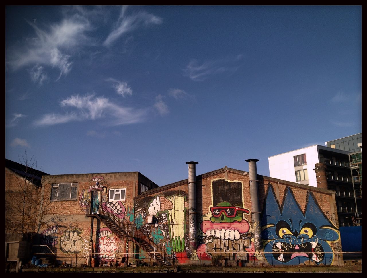 architecture, built structure, building exterior, transfer print, sky, blue, low angle view, auto post production filter, residential structure, residential building, cloud, house, railing, day, building, outdoors, cloud - sky, city, window, graffiti