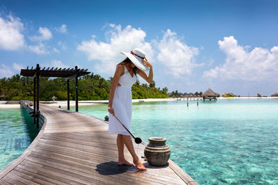 Mid adult woman cleaning leg while standing on pier over sea against sky