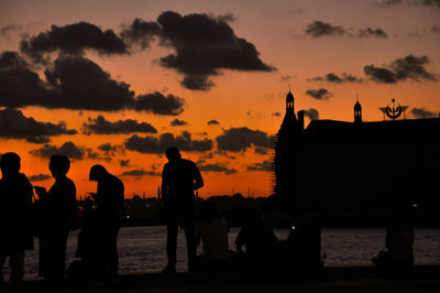 Silhouette people looking at sea during sunset