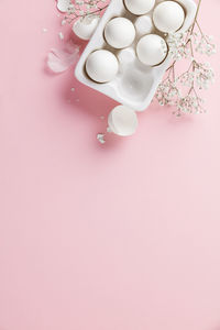 High angle view of eggs in tray by flowers on pink background